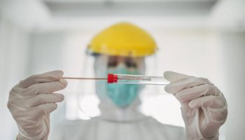 On woman, female doctor in protective suit holding and showing covid-19 tube test and sampling swab.